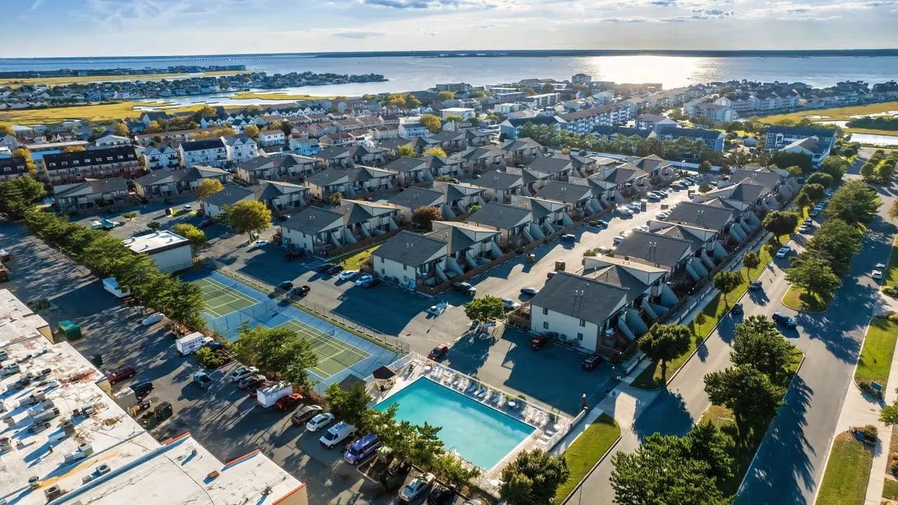 Aerial view of a residential complex with pool and tennis court near a scenic waterfront.